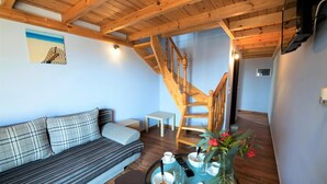 A cozy living room with a sofa, a small table with cups and a remote control, and a wooden staircase. - Argo Maisonettes & Suites (Lefkada)