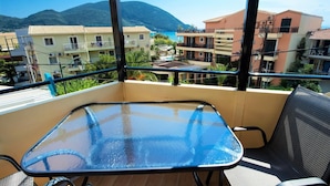 A balcony with a glass table and chairs, overlooking a residential area with buildings and a mountain. - Argo Maisonettes & Suites (Lefkada)