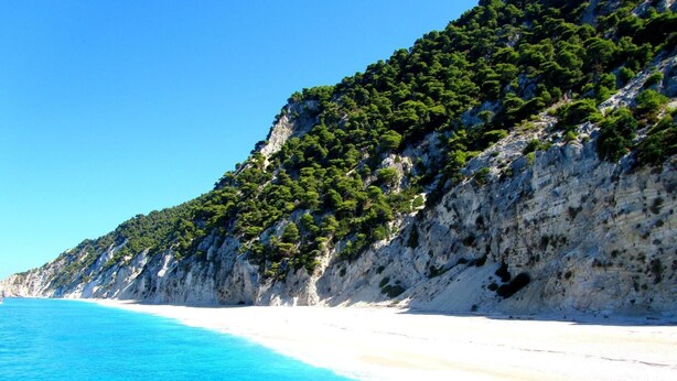 A coastal landscape with a clear blue sea, white sandy beach, and a rocky cliff covered with greenery. - Argo Maisonettes & Suites (Lefkada)