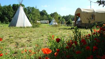 A campsite with a teepee, a covered wagon, and a small cabin.