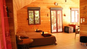Ein gemütliches Blockhaus-Zimmer mit einem Bett, einem kleinen Tisch und einem Stuhl. Zwei Fenster und eine Tür sind vorhanden.