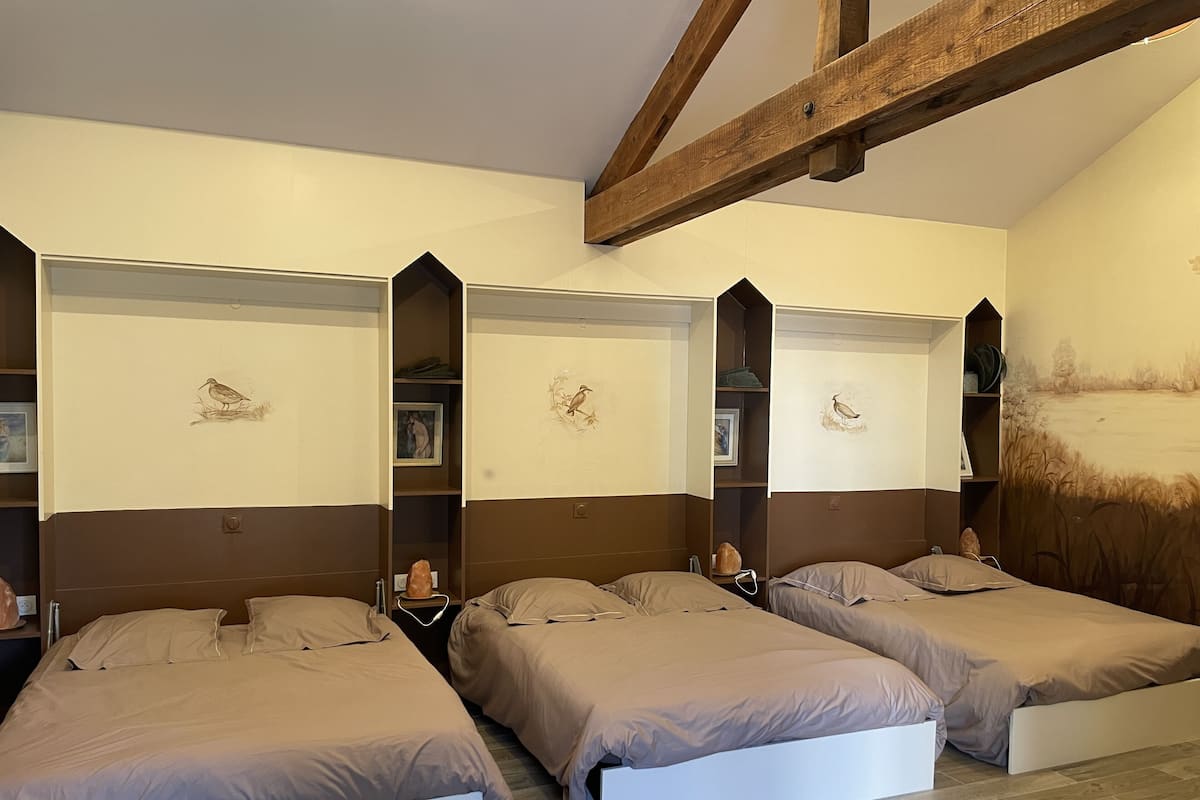 Ein Zimmer mit drei Betten, Holzbalken und Wandbildern.