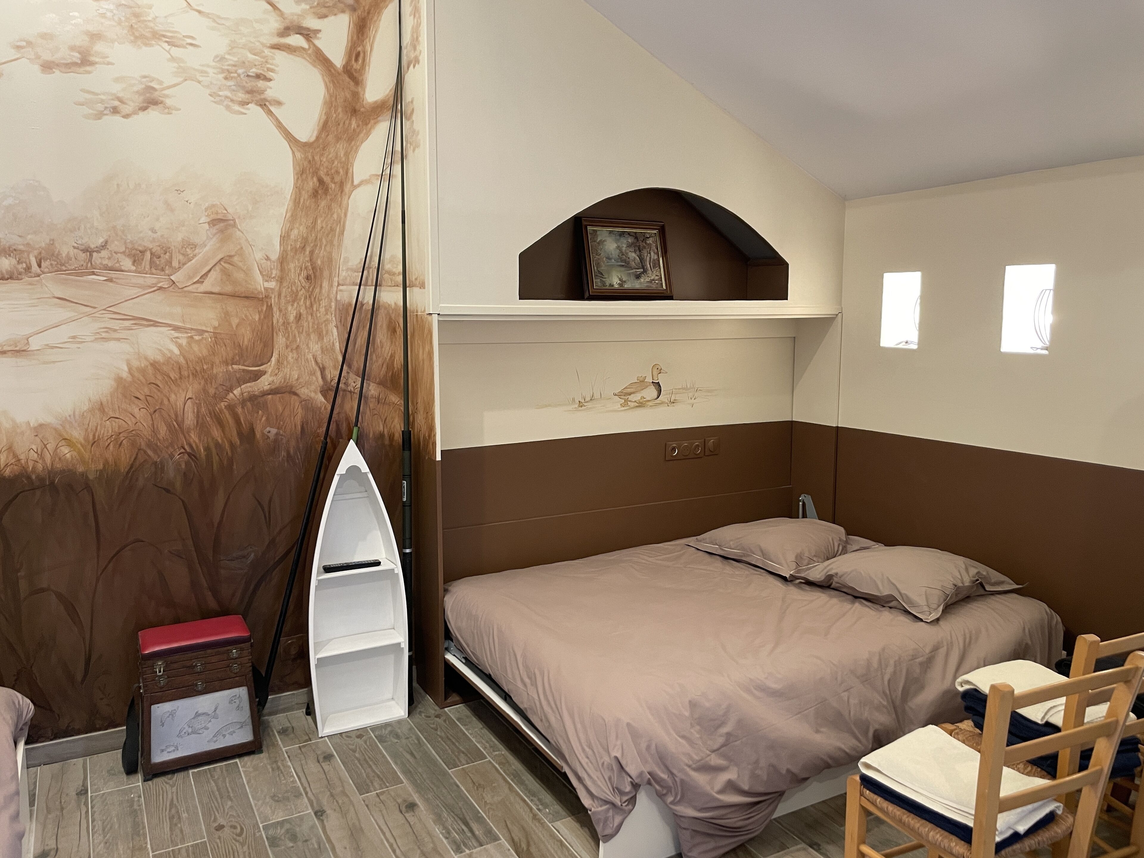 Une chambre à coucher avec un lit, une étagère sur laquelle est posée une image, une petite table et une chaise.