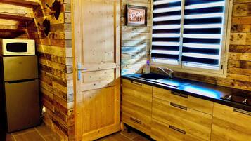 Una cocina con paredes de madera, un refrigerador, un microondas, un lavamanos y una ventana con persianas.