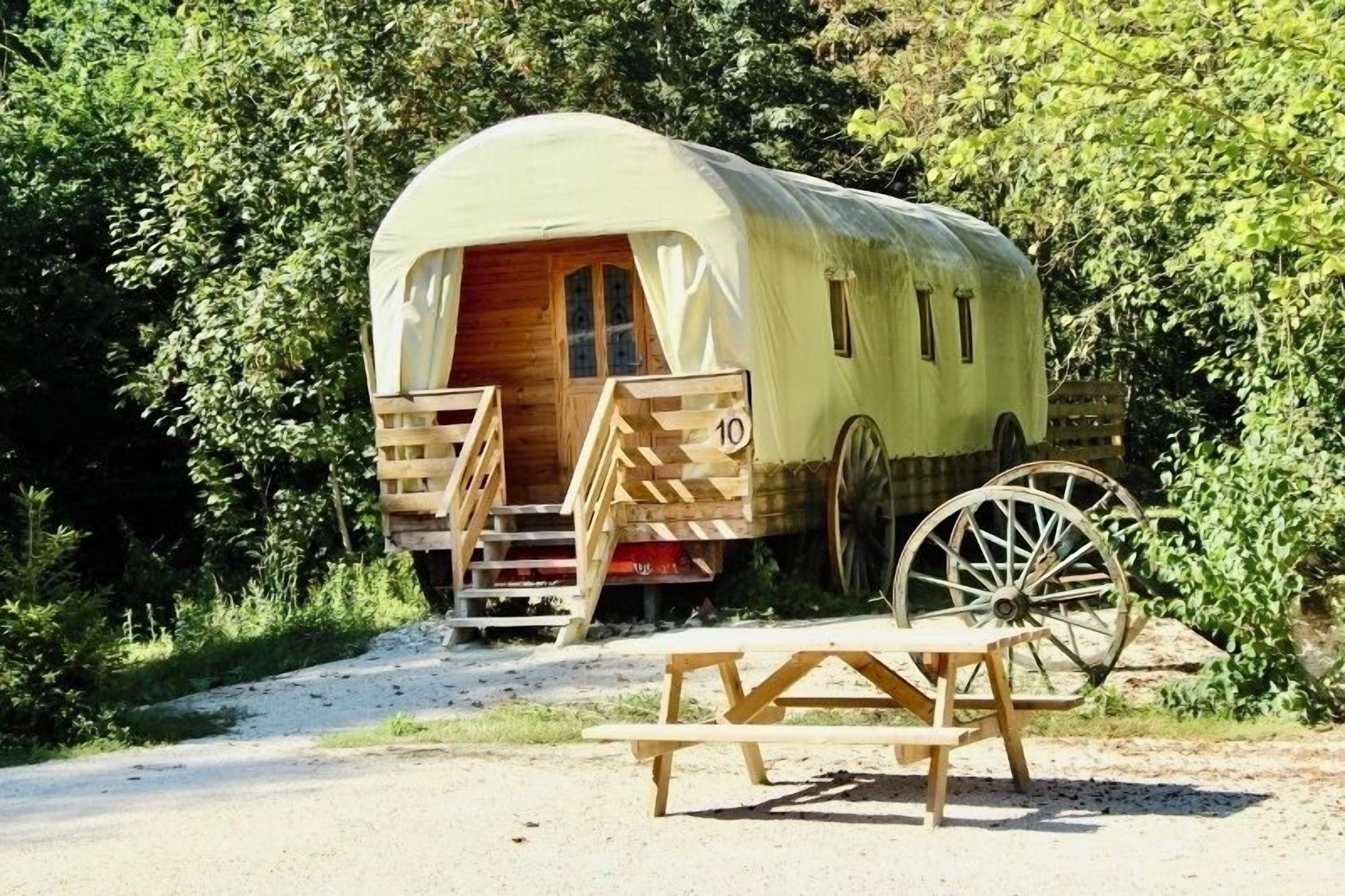 A covered RV with a wooden door and windows, a number '10' on the side, and a wooden picnic table in front.