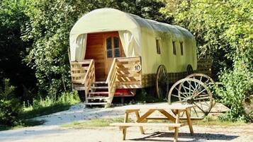 A covered RV with a wooden door and windows, a number '10' on the side, and a wooden picnic table in front.