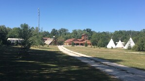 Ein rustikales Gebäude mit rotem Dach, umgeben von einer grünen Wiese und mehreren weißen Tipis.