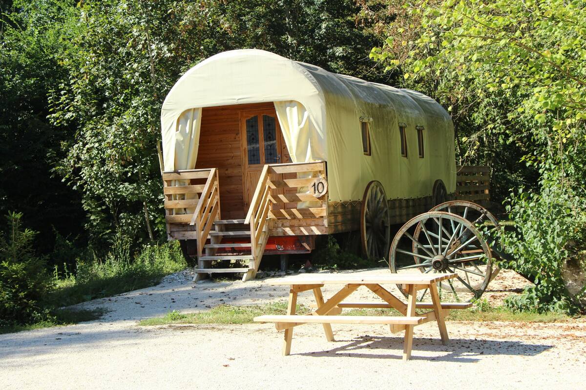 Ein Wohnmobil mit Veranda, Holzinnenausstattung, einem Picknicktisch davor und einem großen, seitlich sichtbaren Rad.