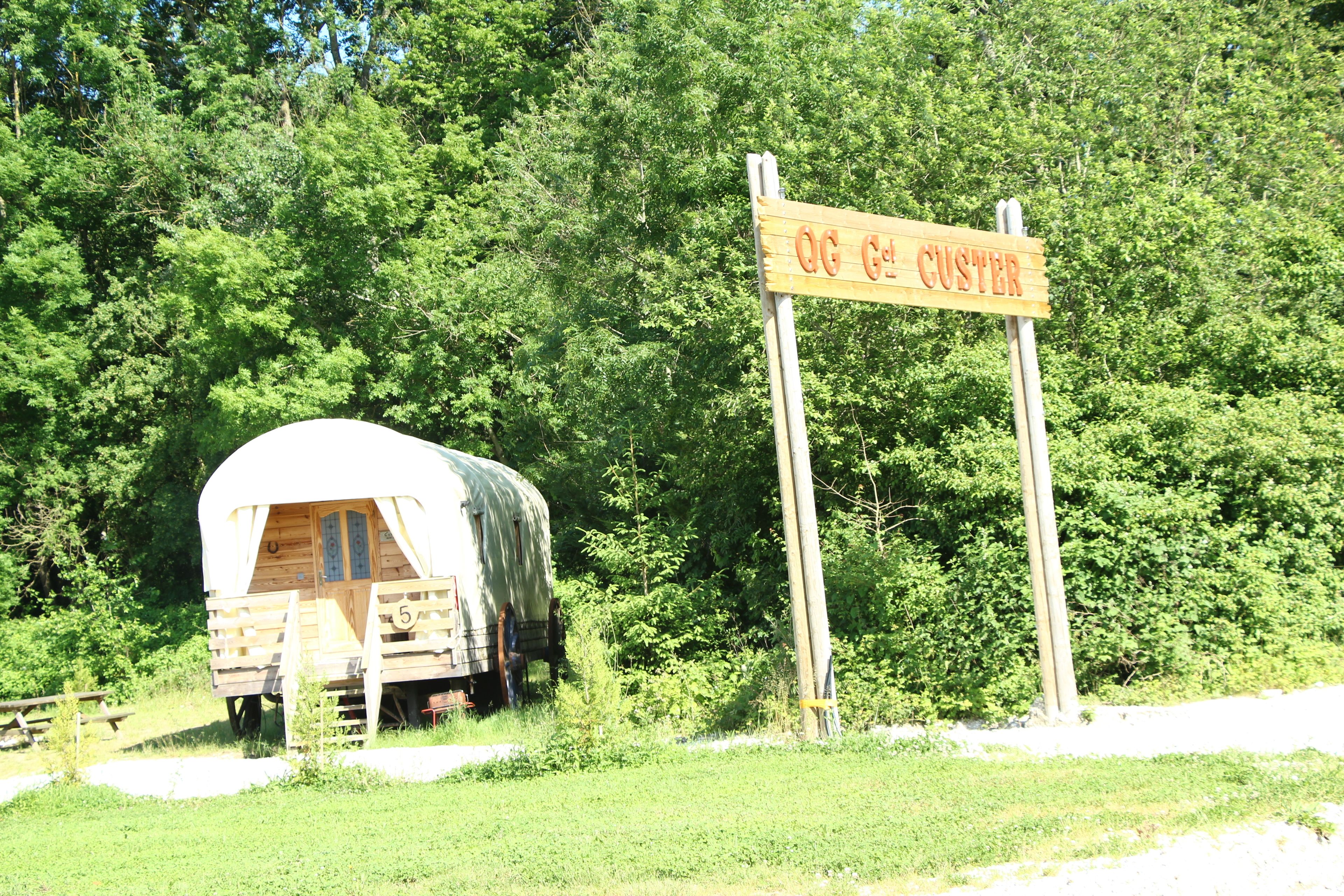 Un panneau en bois sur lequel on peut lire « OG CUSTER », une structure en bois abritée et un paysage boisé en arrière-plan.