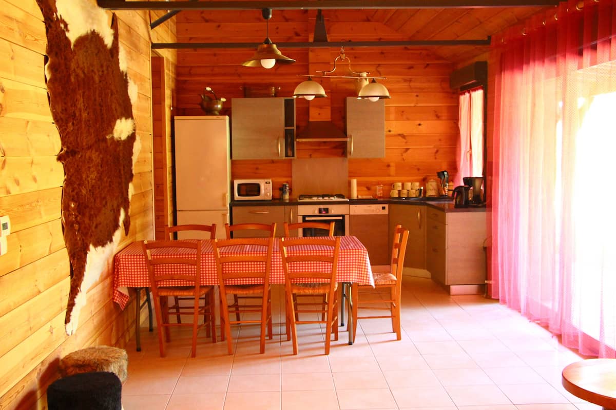 Ein Holzinterieur mit einem Esstisch, der für vier Personen gedeckt ist, einer Küchenzeile mit Geräten und einem großen Fellteppich an der Wand.