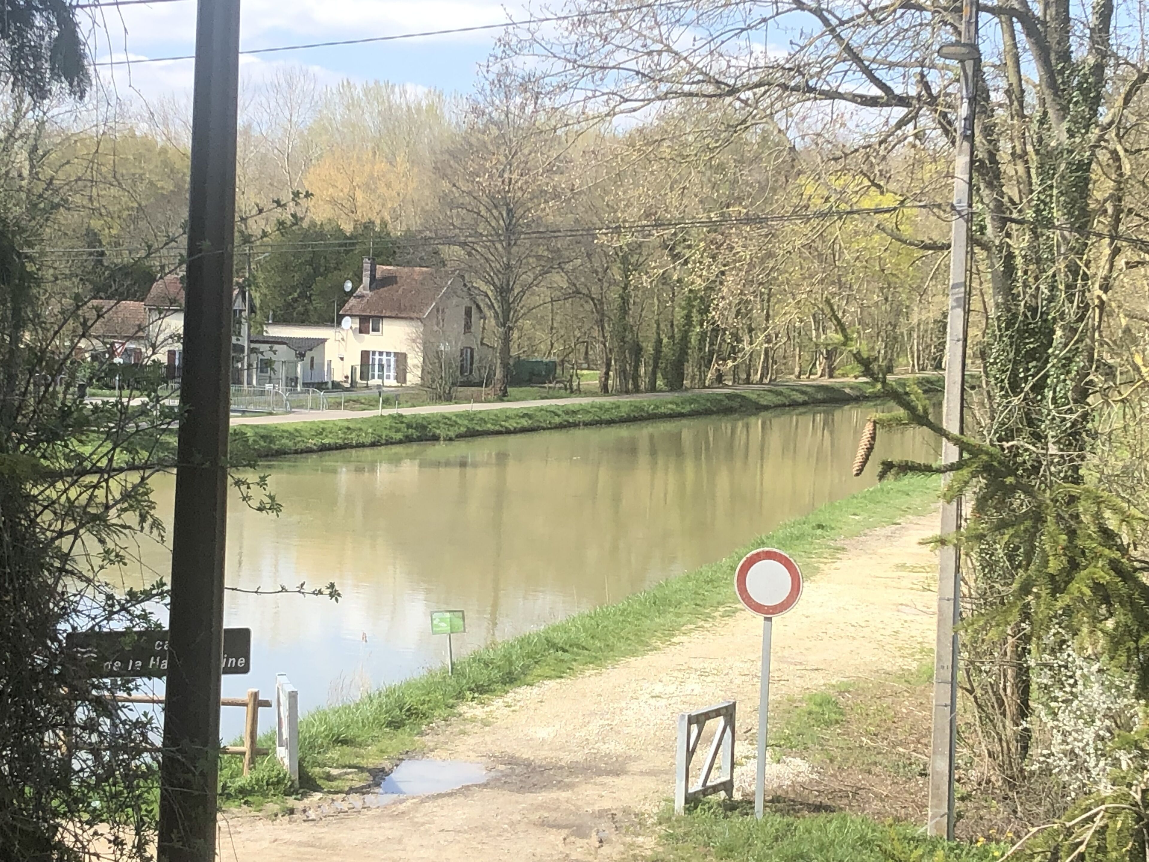 Une rivière, avec des maisons d’un côté et un panneau indiquant l’interdiction d’accès de l’autre.