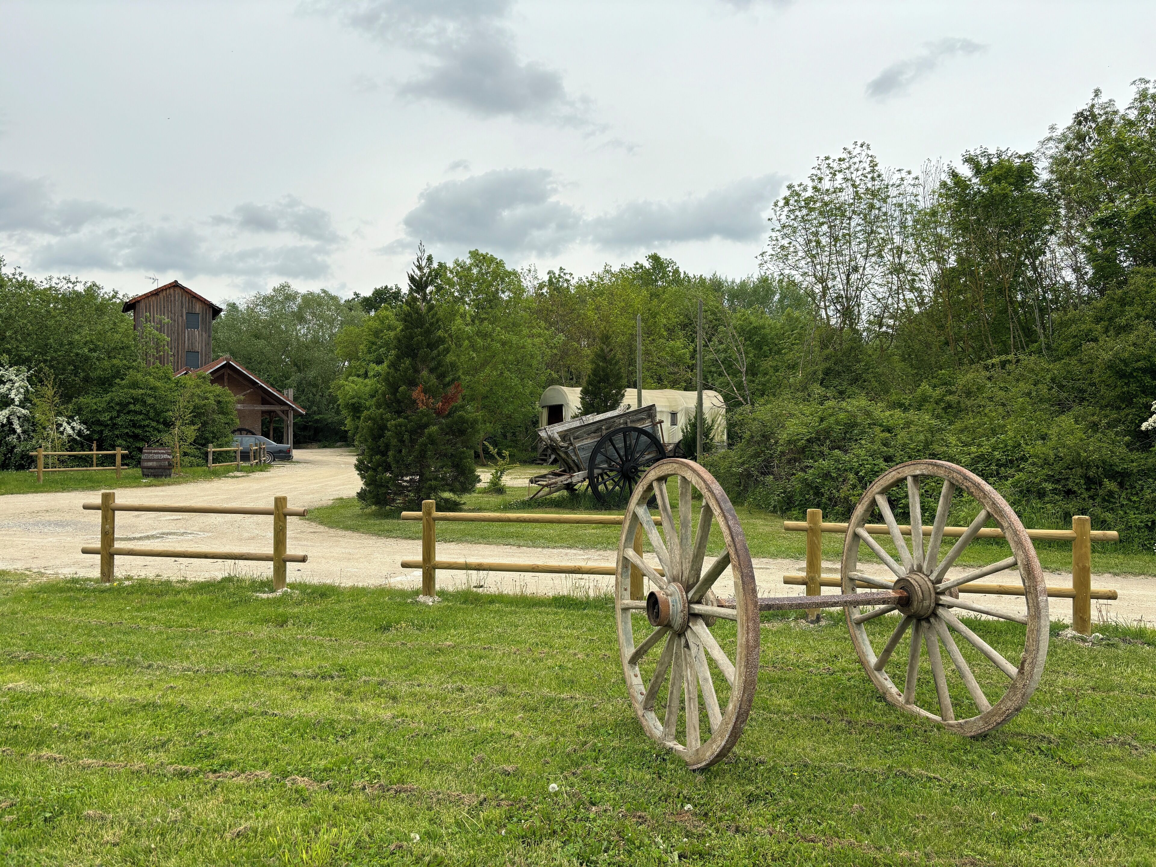 A rustic outdoor setting with a wooden wagon, a barn, and a dirt path.