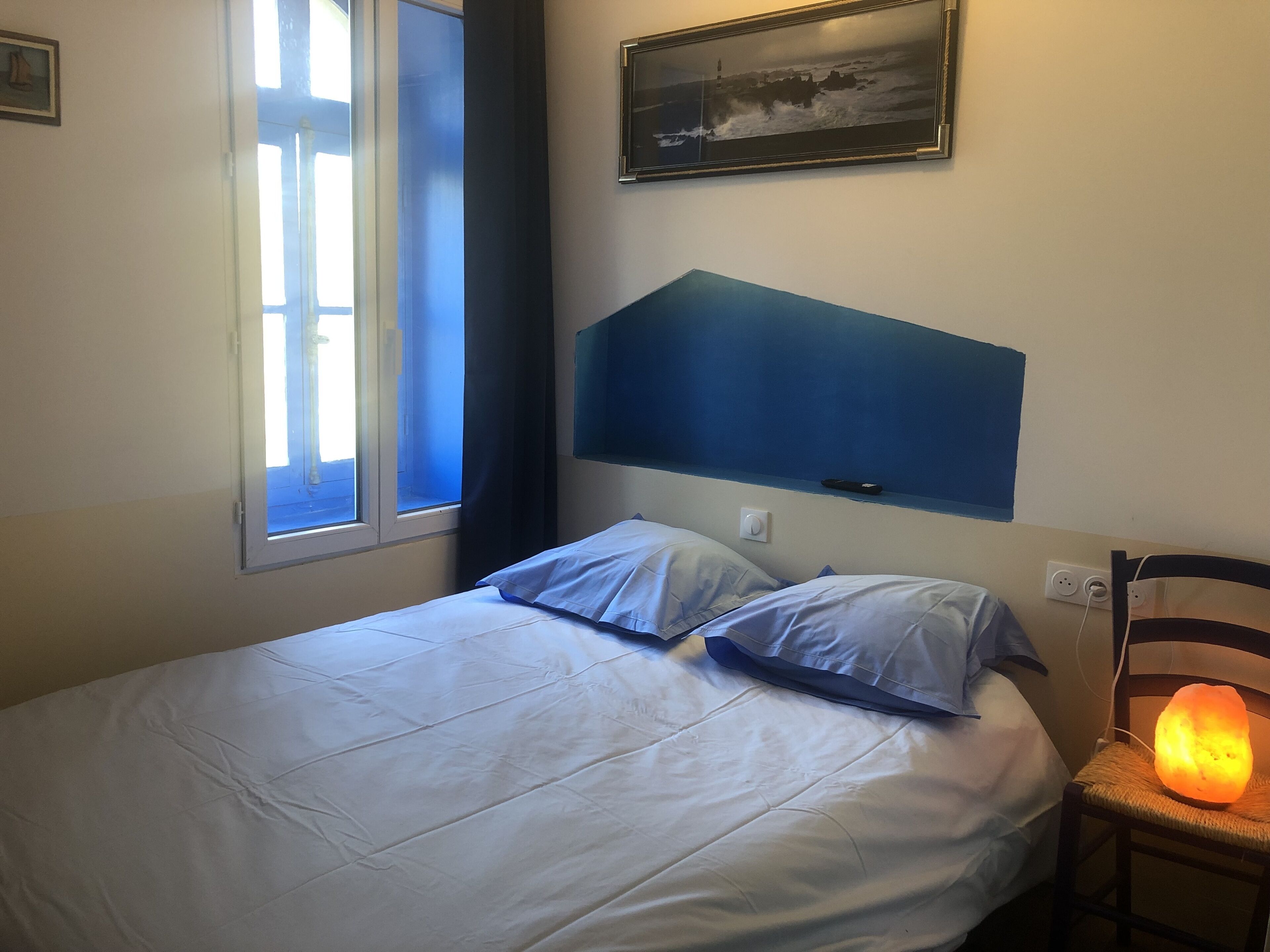 Un dormitorio con cama, ventana, calentador de pared y un cuadro.