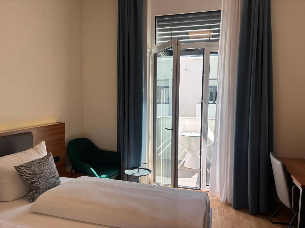 A hotel room with a bed, a small table, a chair, and a balcony with a glass door.