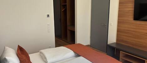 Una habitación de hotel con una cama, un armario, un televisor y una puerta.