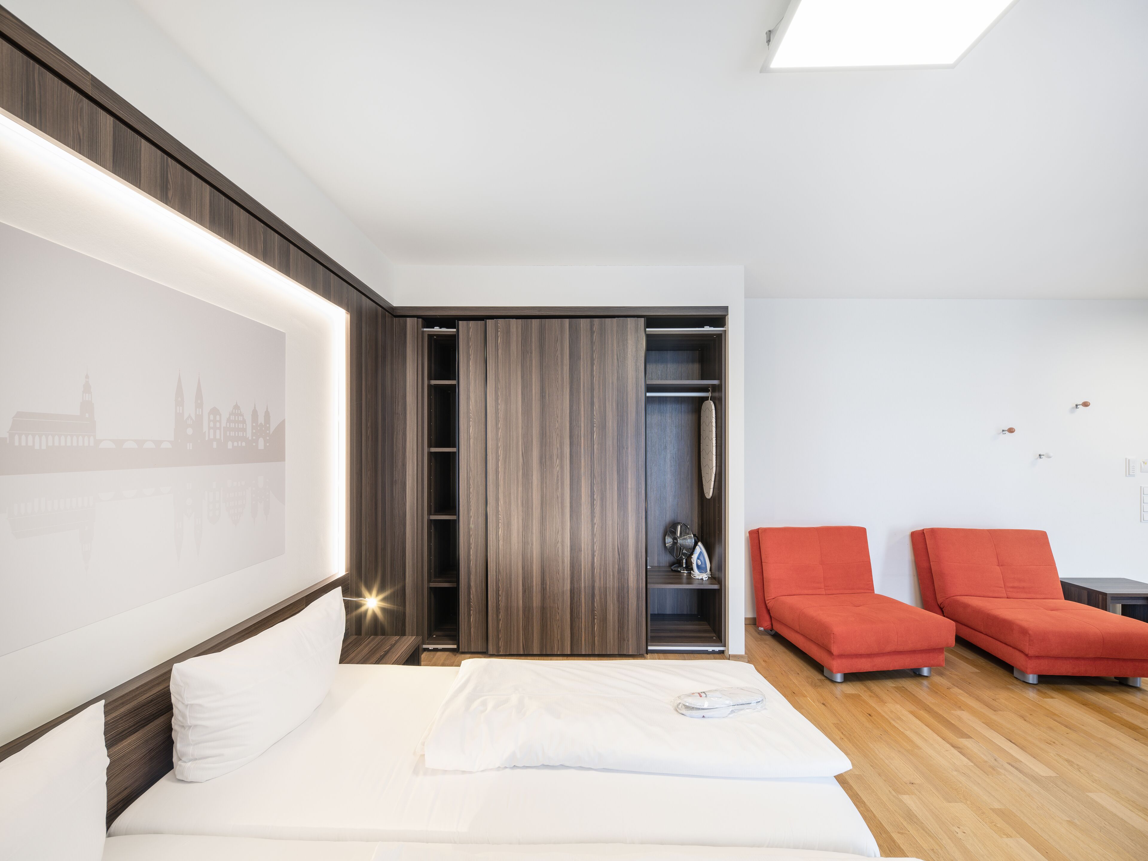Una habitación de hotel moderna con cama, armario y dos sillones rojos.