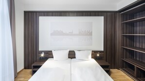 Et moderne hotelværelse med en stor seng, et bybillede som kunst på væggen og en indbygget reol.