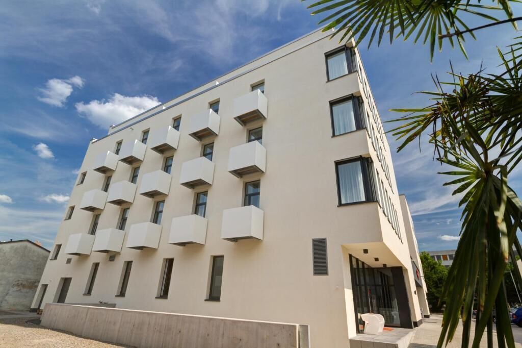 A modern building with a flat facade, multiple balconies, and a clear sky.