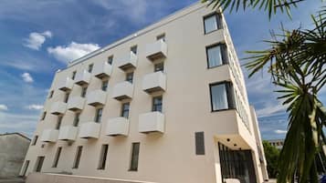 A modern building with a flat facade, multiple balconies, and a clear sky.