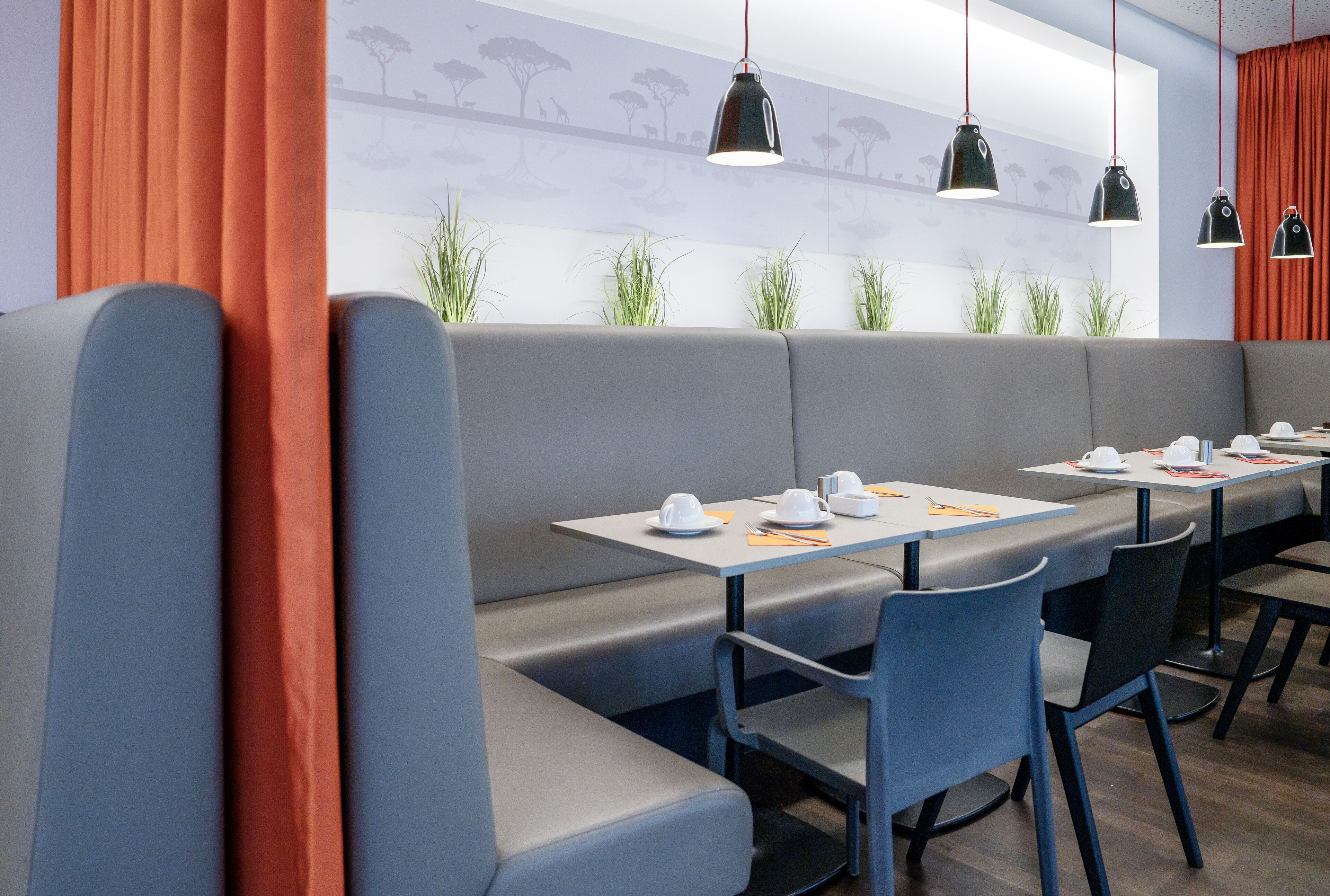Ein modernes Restaurant mit grauen Sitzecken, schwarzen Pendelleuchten und einem Wandgemälde.