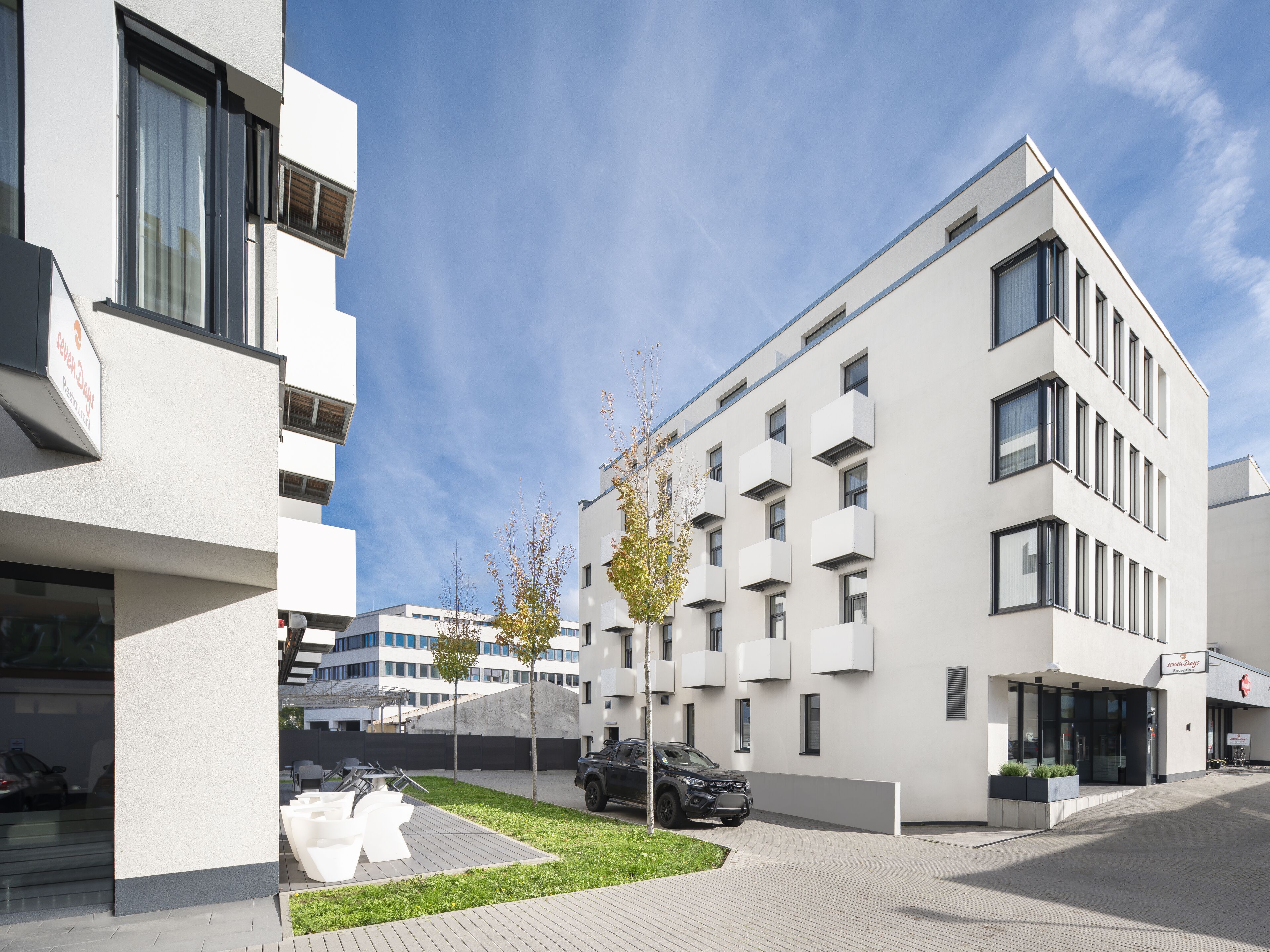 Een modern gebouw met een platte gevel, grote ramen en een parkeerplaats met enkele auto's.
