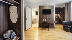 En moderne stue med trægulv, et fladskærms-tv på væggen, et spiseområde med bord og stole, samt en lædersofa.
