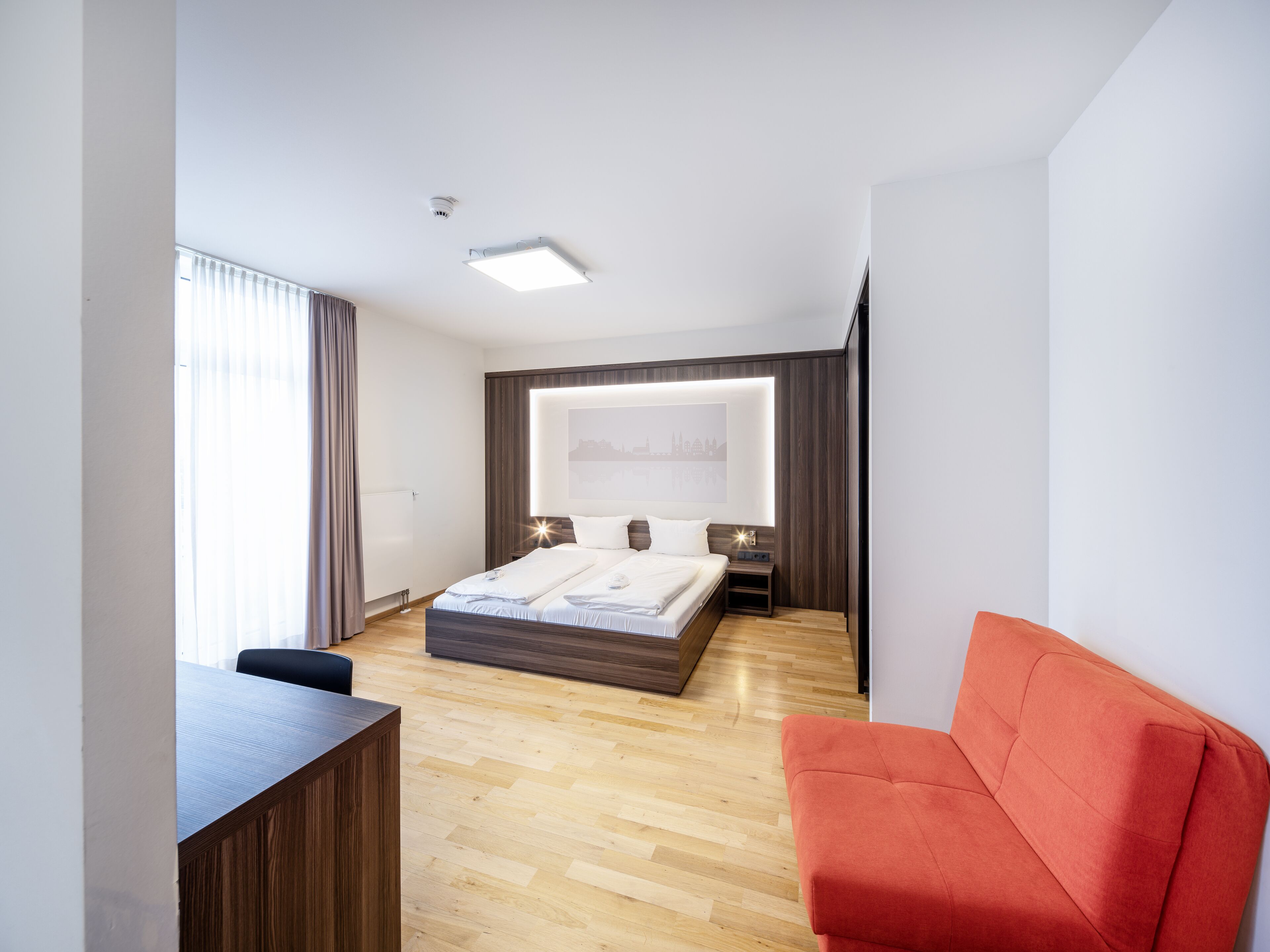 Een moderne hotelkamer met een groot bed, een bureau en een rode bank.