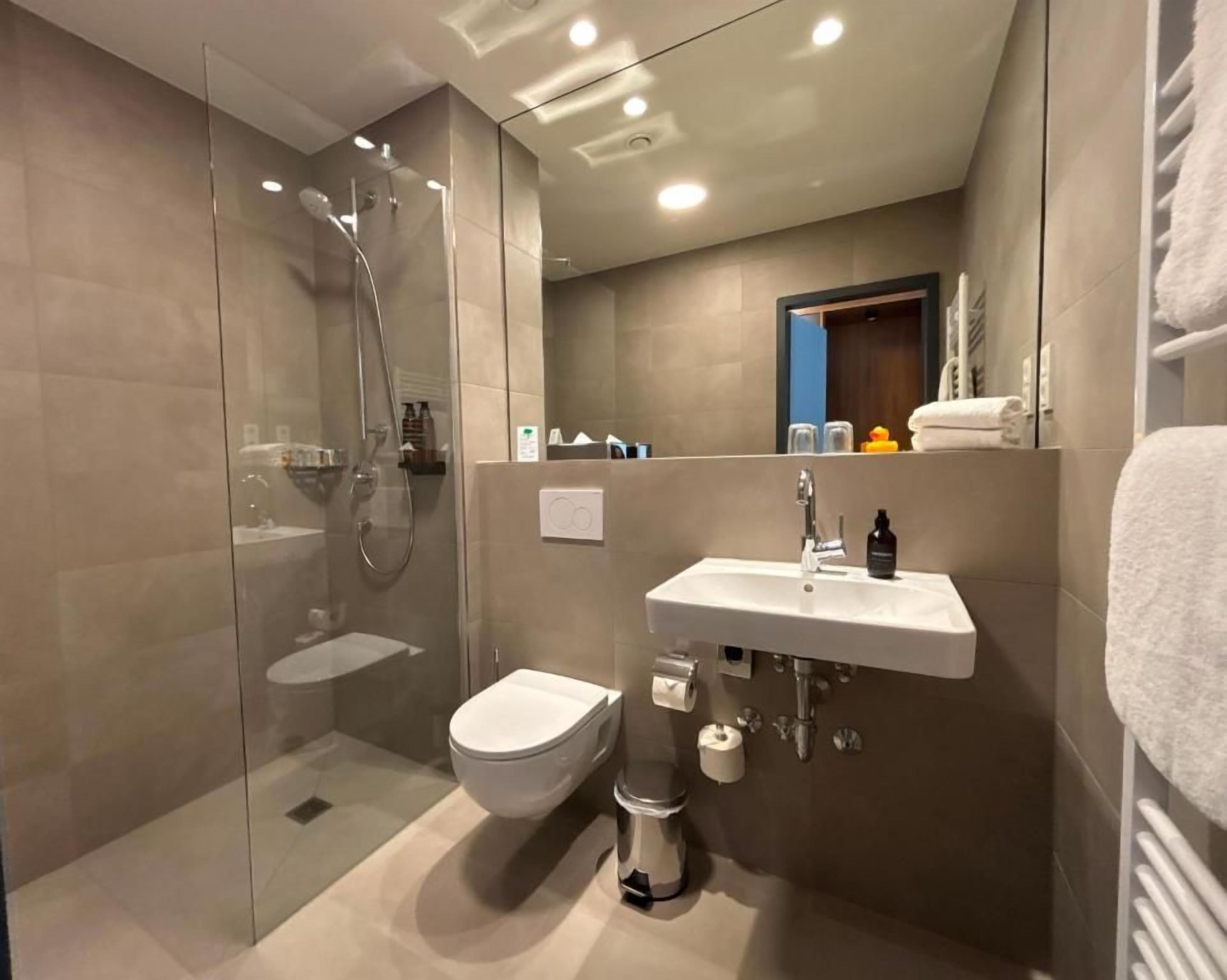 A modern bathroom with a glass-enclosed shower, a white toilet, a sink with a mirror, and a towel rack.