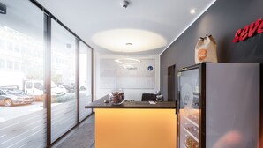 Et moderne receptionsområde med en glasdør, en receptionsdisk, et køleskab og et skilt på væggen.