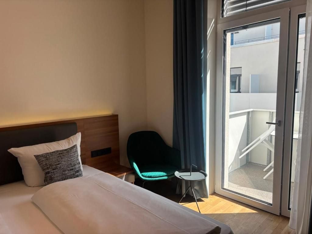Habitación de hotel con cama, una silla, una mesita y vistas al balcón exterior.