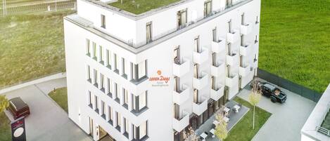 A modern hotel with a flat roof, multiple balconies, and a parking area.