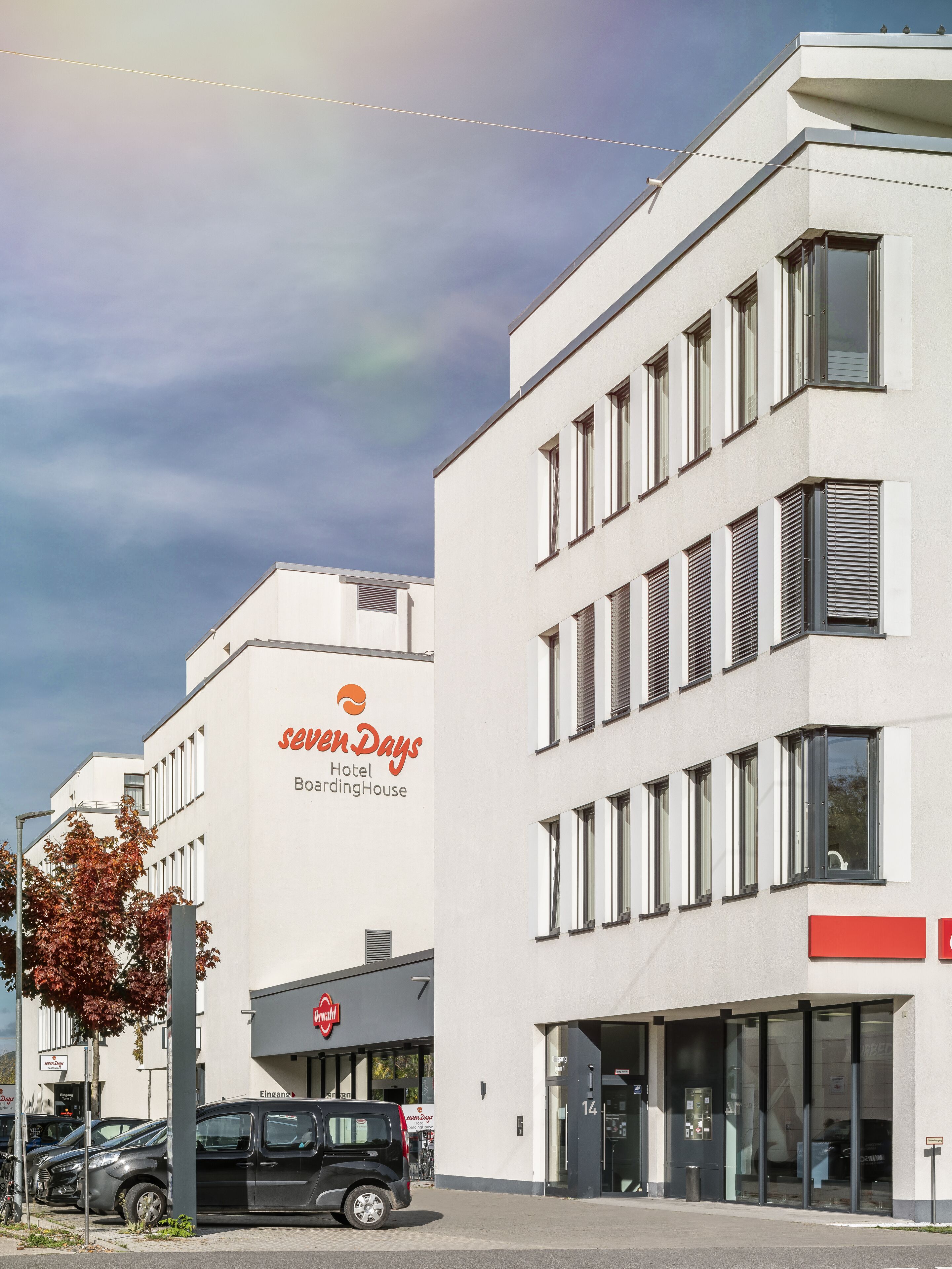 A modern hotel building with a sign for 'sevenDays Hotel BoardingHouse'.