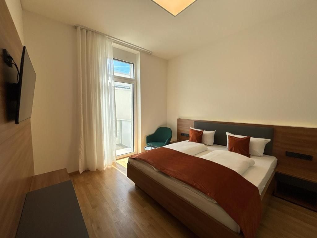 A hotel room with a bed, a chair, a TV, and a window with curtains.