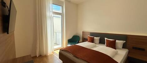 A hotel room with a bed, a chair, a TV, and a window with curtains.