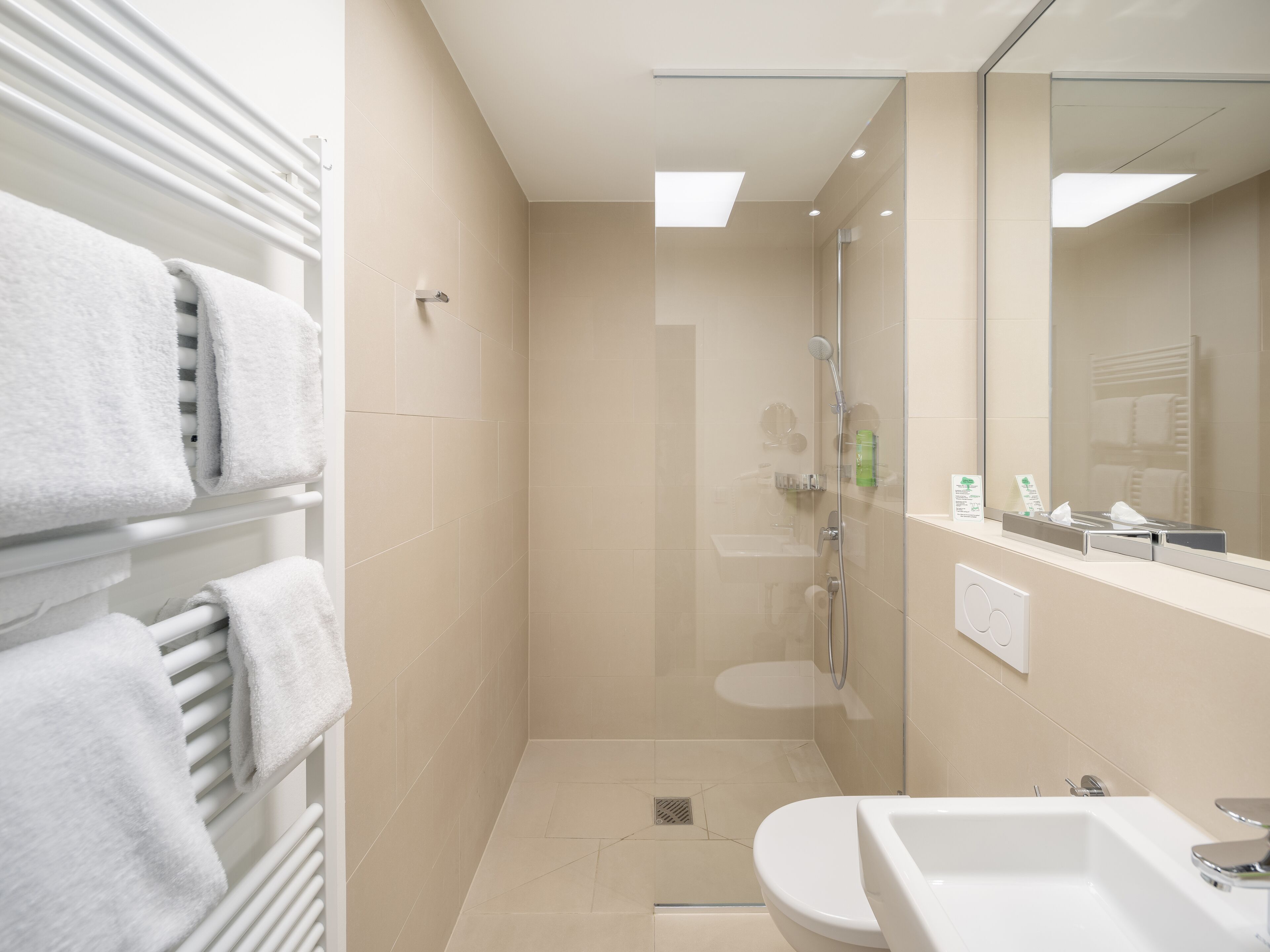 A modern bathroom with a glass shower enclosure, a white sink, and a towel rack with neatly folded towels.