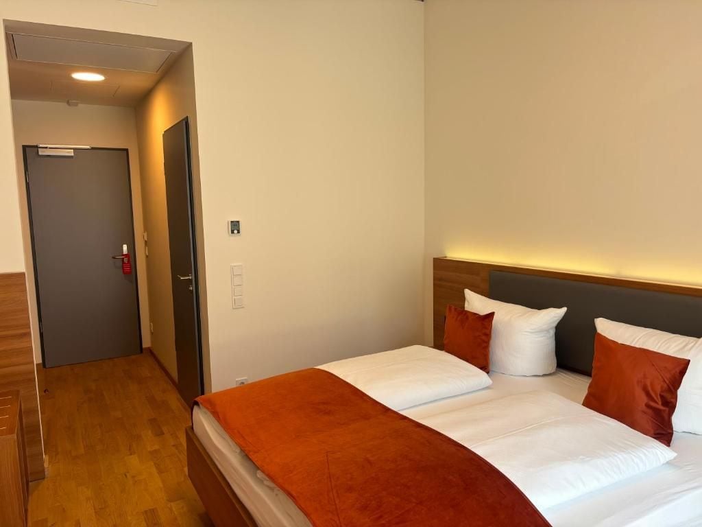 A hotel room with a bed, a wooden floor, a door, and a light fixture.