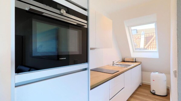 A modern kitchen with a built-in oven, a window with a view, and a compact countertop. - Apartment Traveblick (Lübeck)
