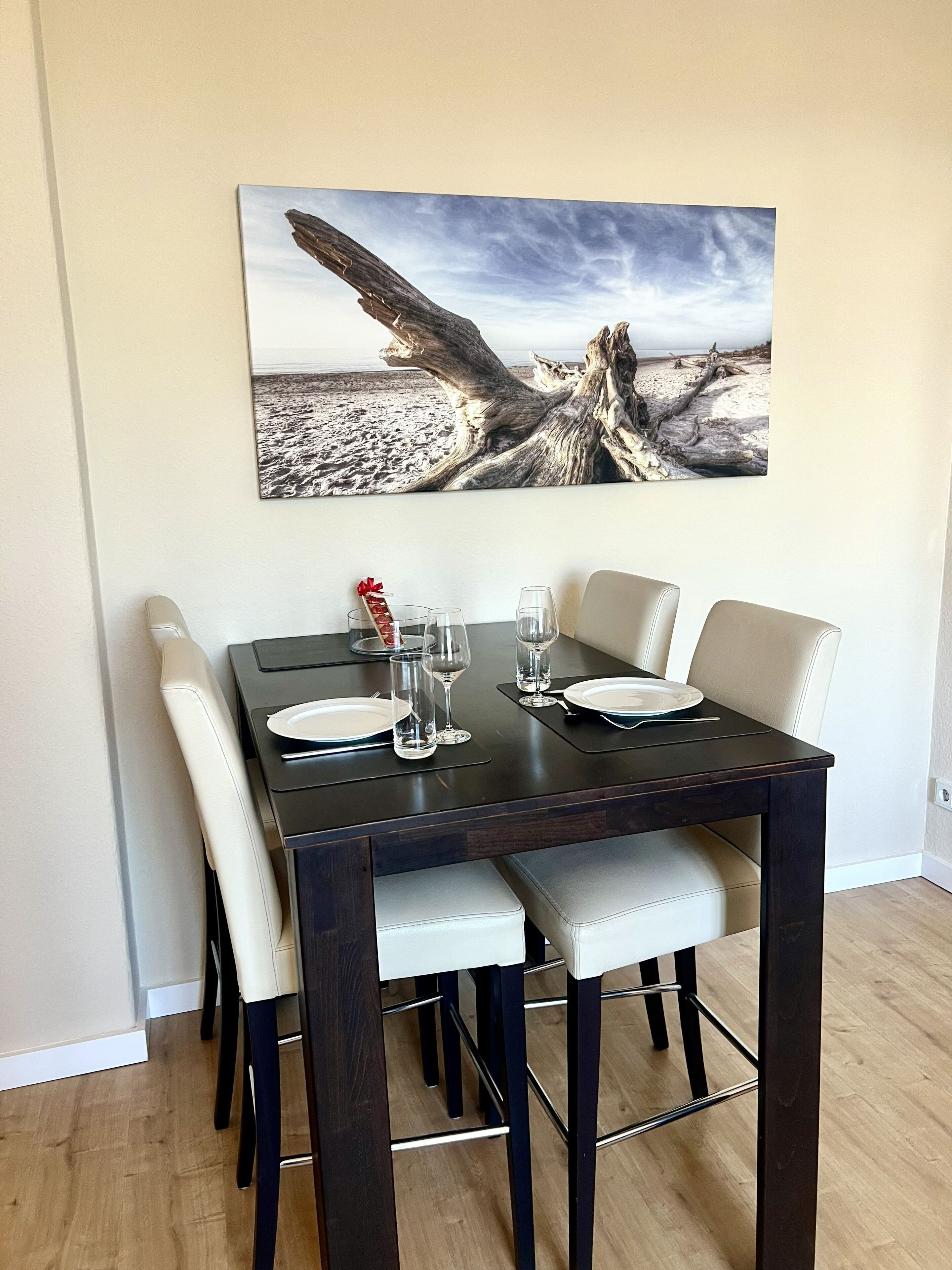Un tavolo da pranzo con quattro sedie, un quadro incorniciato con un paesaggio costiero e un piccolo oggetto decorativo.