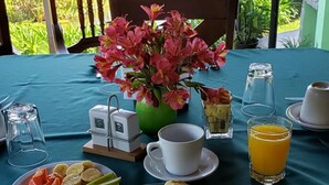 Une table de petit-déjeuner avec des assiettes d’œufs, de saucisses et de fruits, un vase de fleurs et une vue sur un étang.