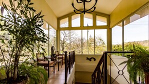 Une véranda spacieuse avec de grandes fenêtres, un escalier en bois et diverses plantes d’intérieur.