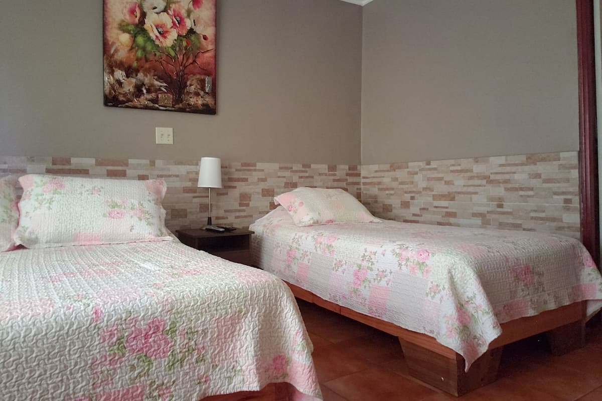 Une chambre d’hôtel avec deux lits, chacun agrémenté d’une literie à motifs floraux, une table de chevet avec une lampe et un tableau au mur.