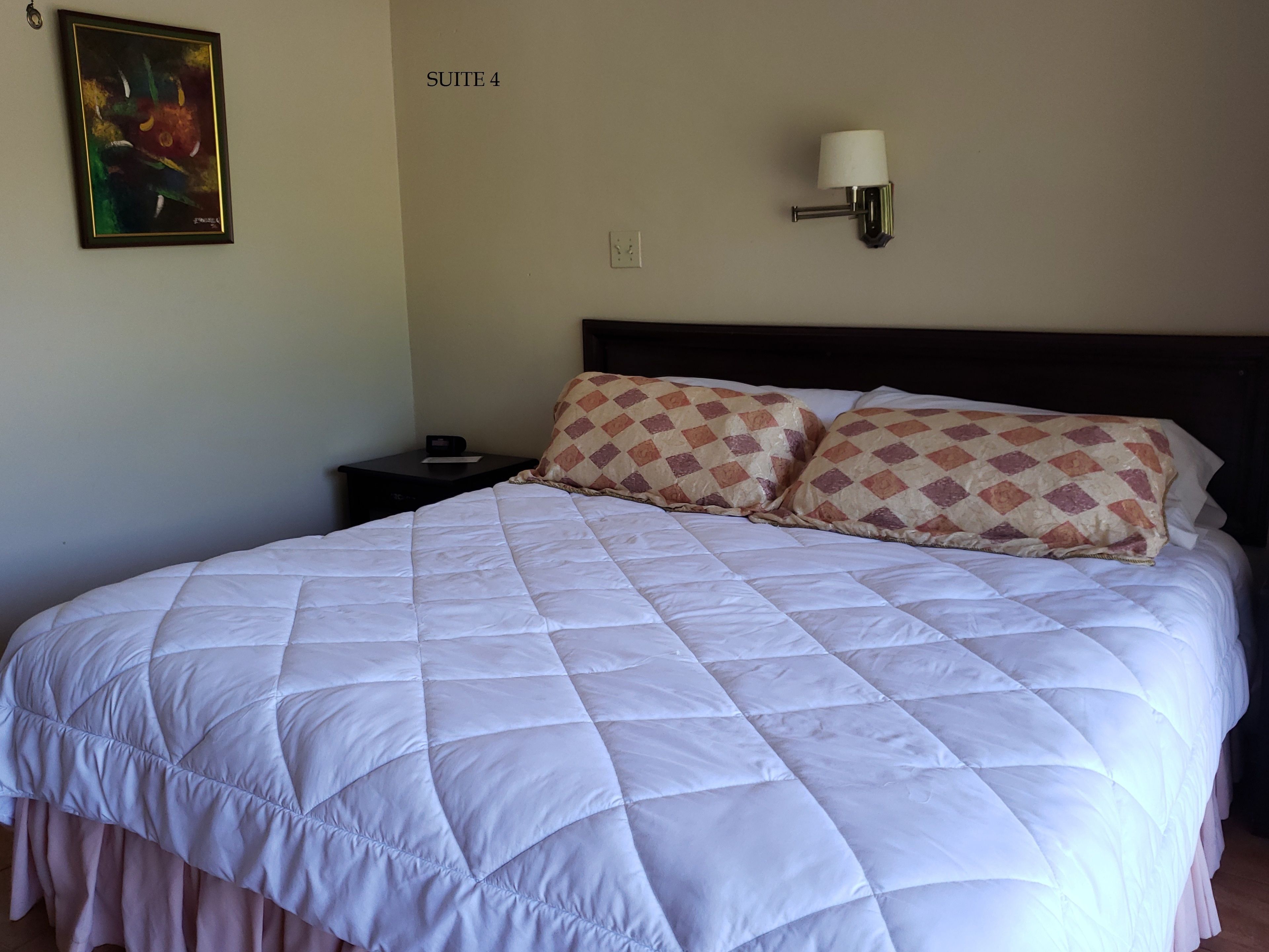 Een hotelkamer met een groot bed, een nachtkastje, een wandlamp en een schilderij aan de muur.