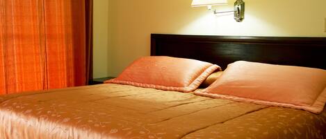 Una cama bien hecha con una colcha de estampado floral y dos almohadas a juego, una lámpara de pared y un cabecero de madera.