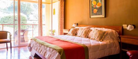 A bedroom with a bed, a chair, a nightstand, a wall-mounted lamp, and a window with curtains.