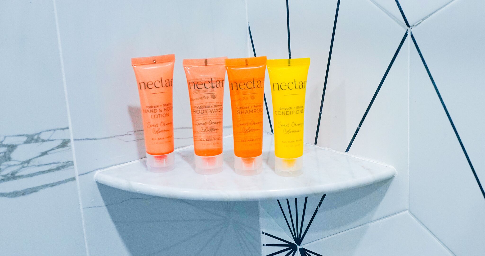 Four tubes of nectar products on a white shelf against a tiled wall.