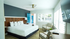 A modern hotel room with a large bed, a desk with a remote control, a chair, and a ceiling fan. - Ivory Sands Beach Suites (Clearwater Beach)