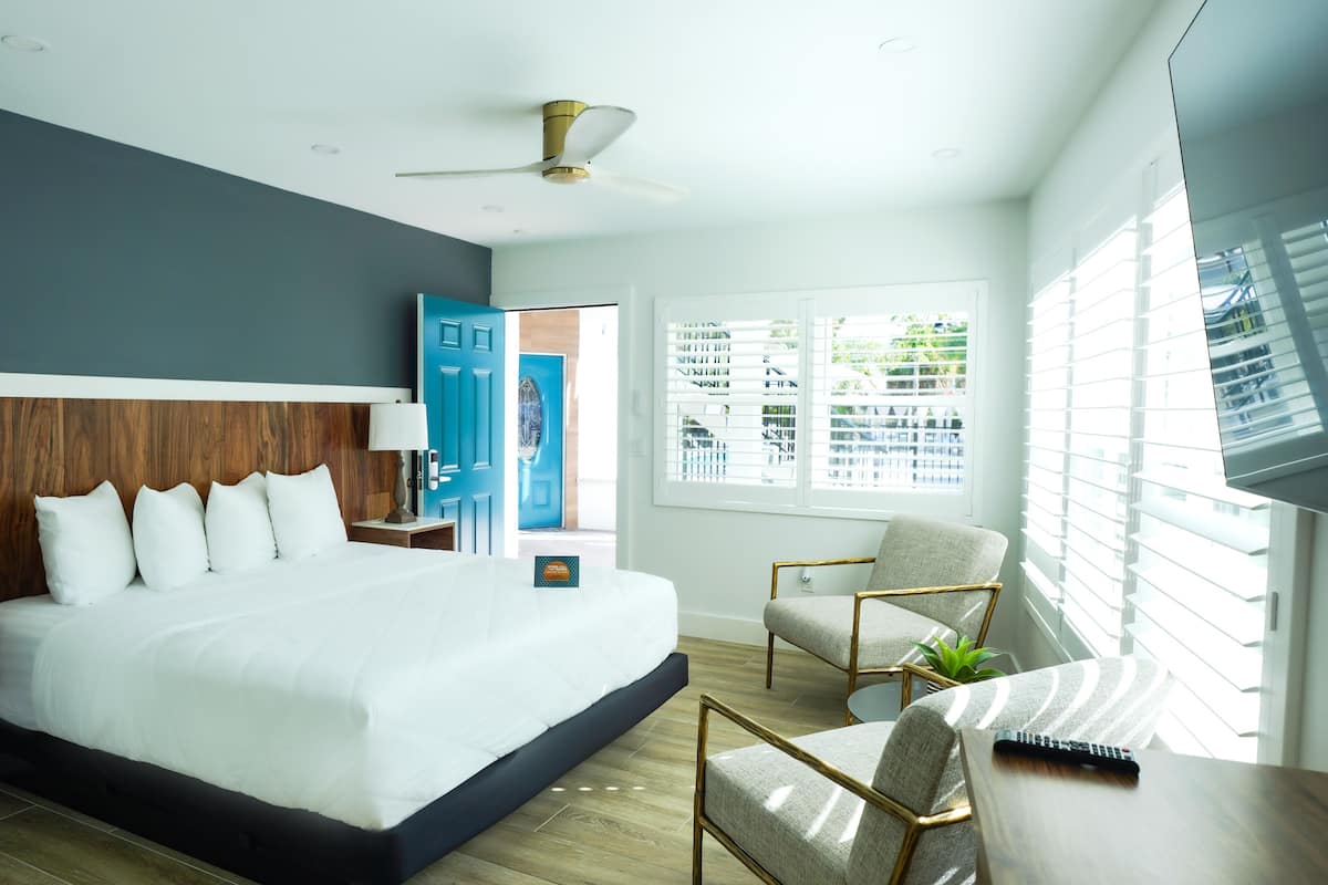Quarto de hotel moderno com uma cama grande, uma escrivaninha com controle remoto, uma cadeira e um ventilador de teto.