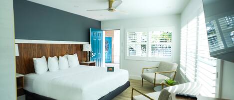 A modern hotel room with a large bed, a desk with a remote control, a chair, and a ceiling fan.