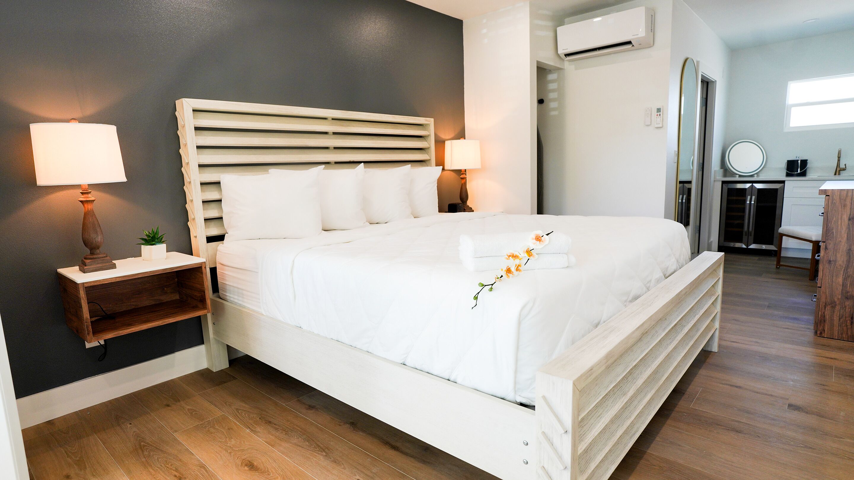 Una camera da letto ordinata con un letto grande, due comodini con lampade, una piccola pianta e un condizionatore d'aria a parete.