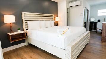 Una camera da letto ordinata con un letto grande, due comodini con lampade, una piccola pianta e un condizionatore d'aria a parete.